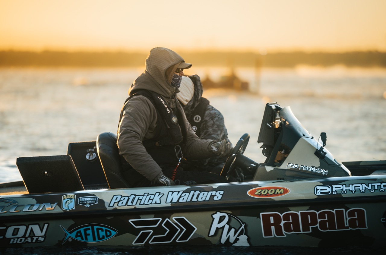 An angler on a boat that is covered in brand sponsor stickers.