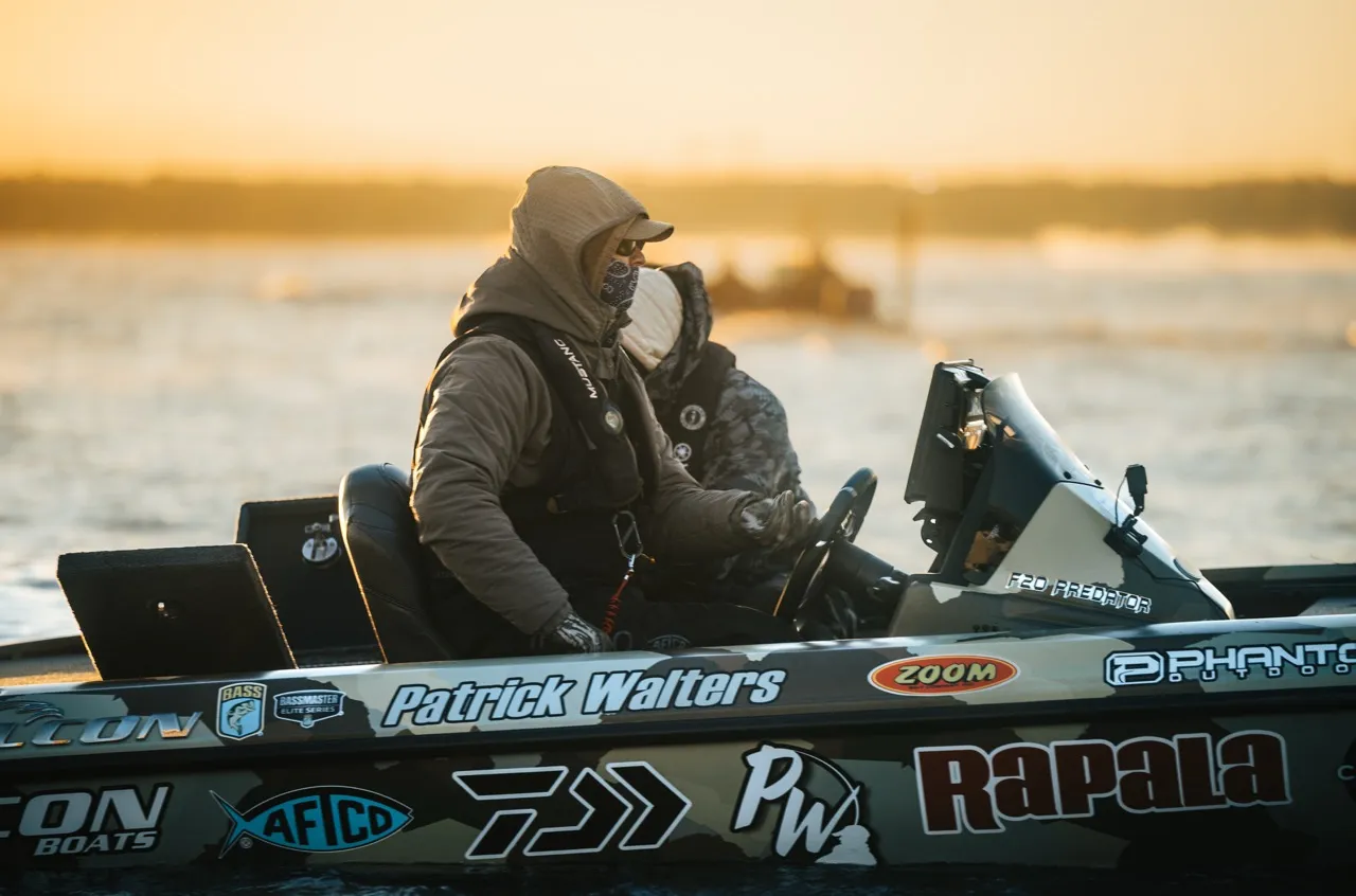 An angler on a boat that is covered in brand sponsor stickers.
