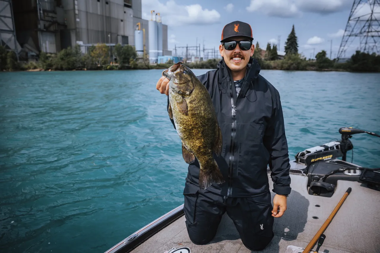 An angler on the water, holding up a largemouth bass. 
